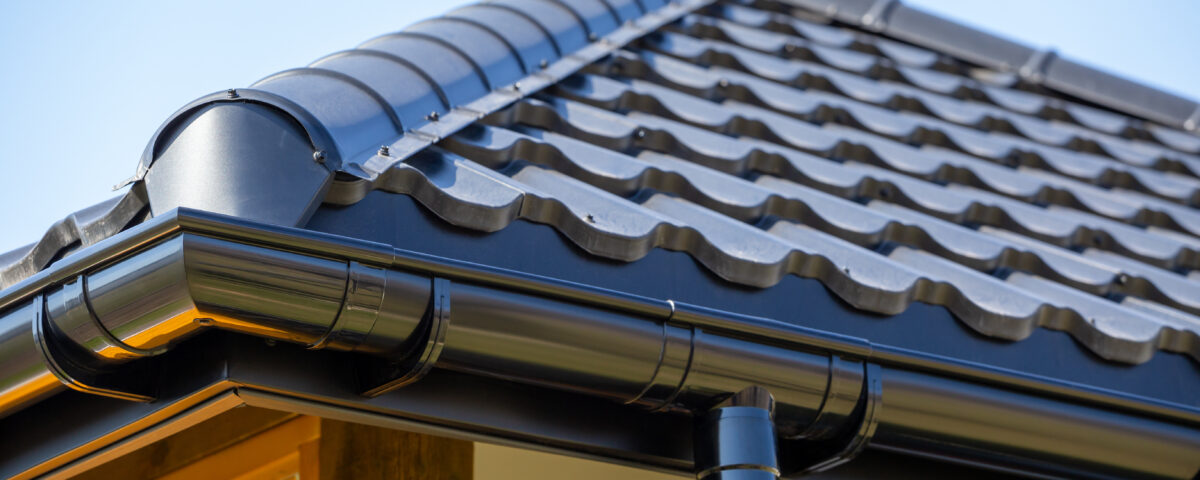 Corner of the new modern house with roof, gutter and wooden shutter under blue sky