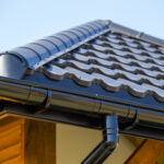 Corner of the new modern house with roof, gutter and wooden shutter under blue sky